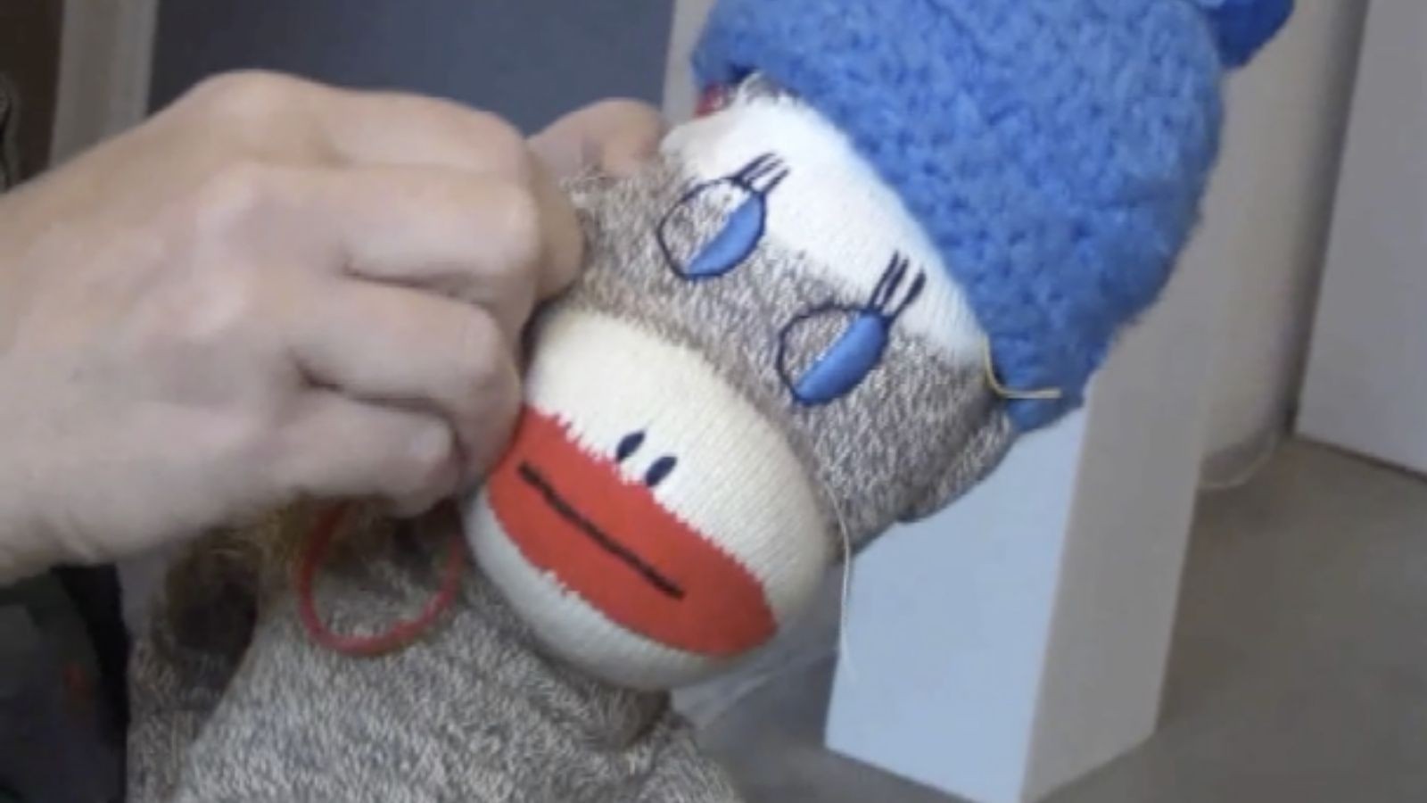Close-up of hands repairing a sock monkey's cheek in a still from Stab by Nayland Blake
