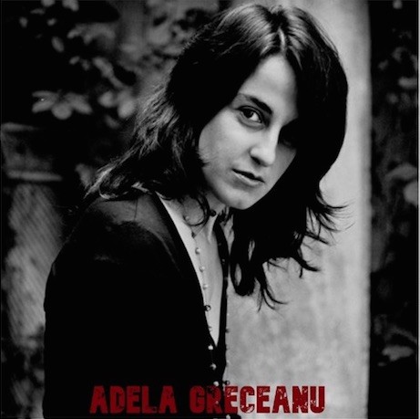 In this black and white portrait, Adela Greceanu looks at the camera from the side, standing in front of a wall with vines