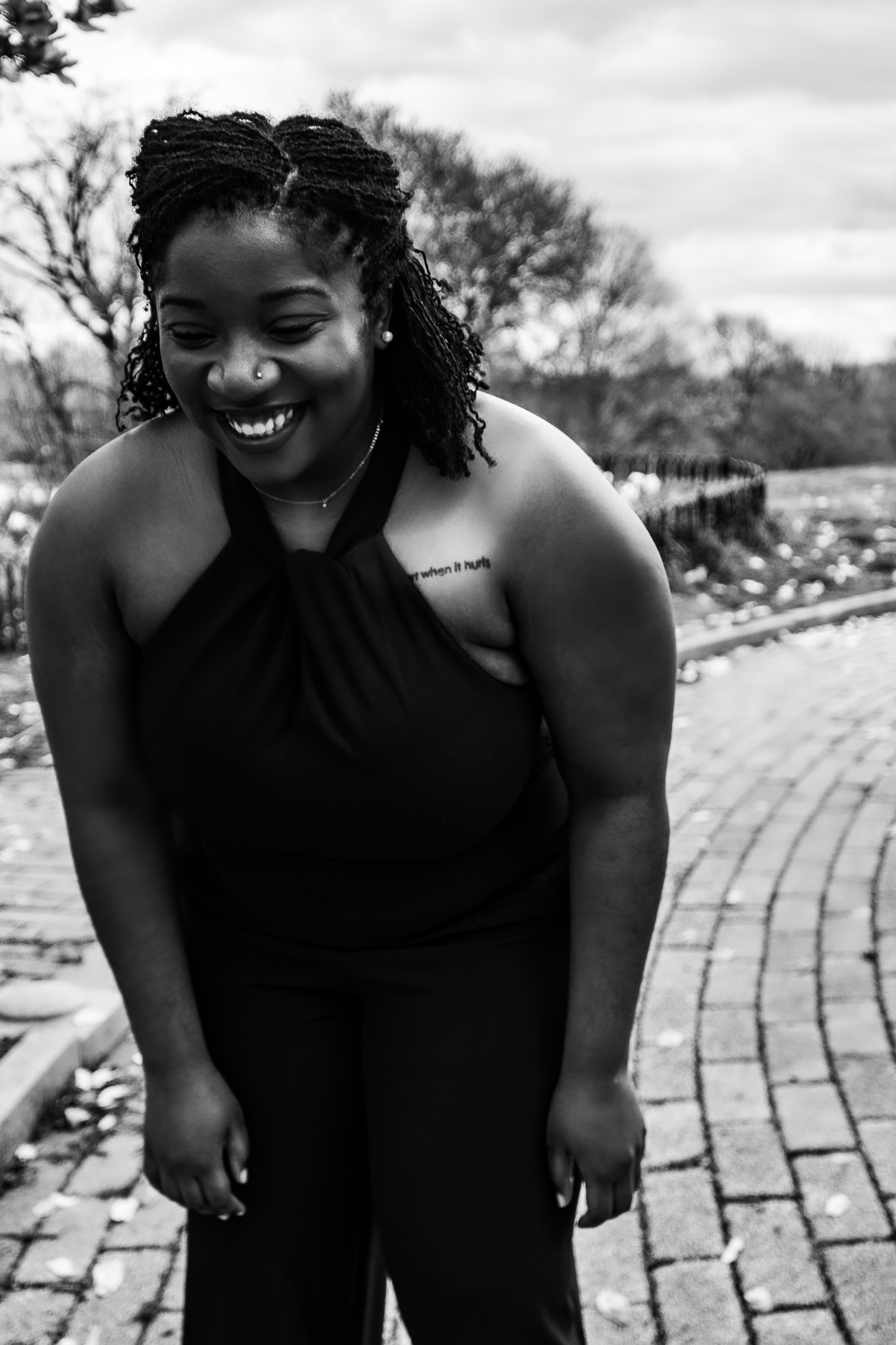 In this black and white portrait, Brendane Tynes is laughing, standing on a brick path.