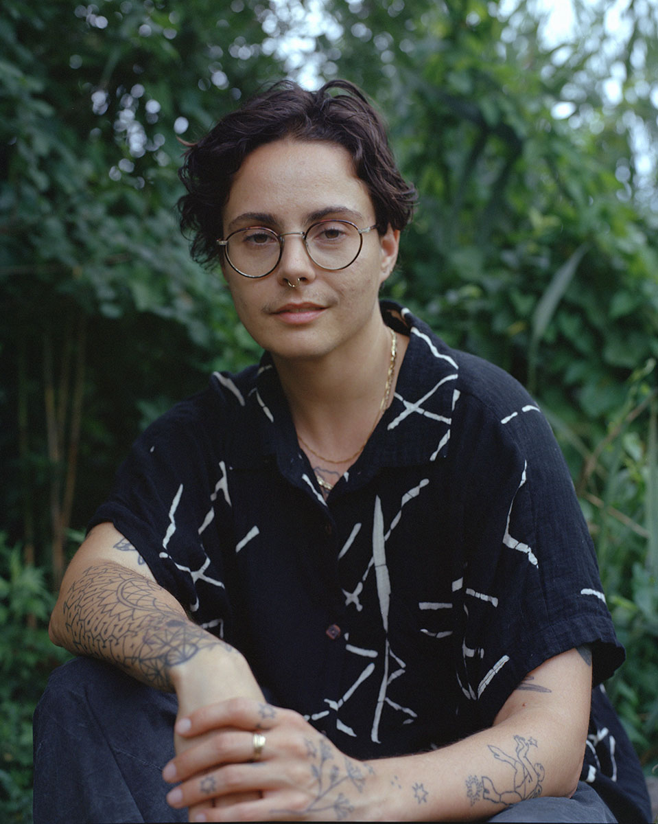 charles is seated in a leafy environment, wearing a black and white shirt