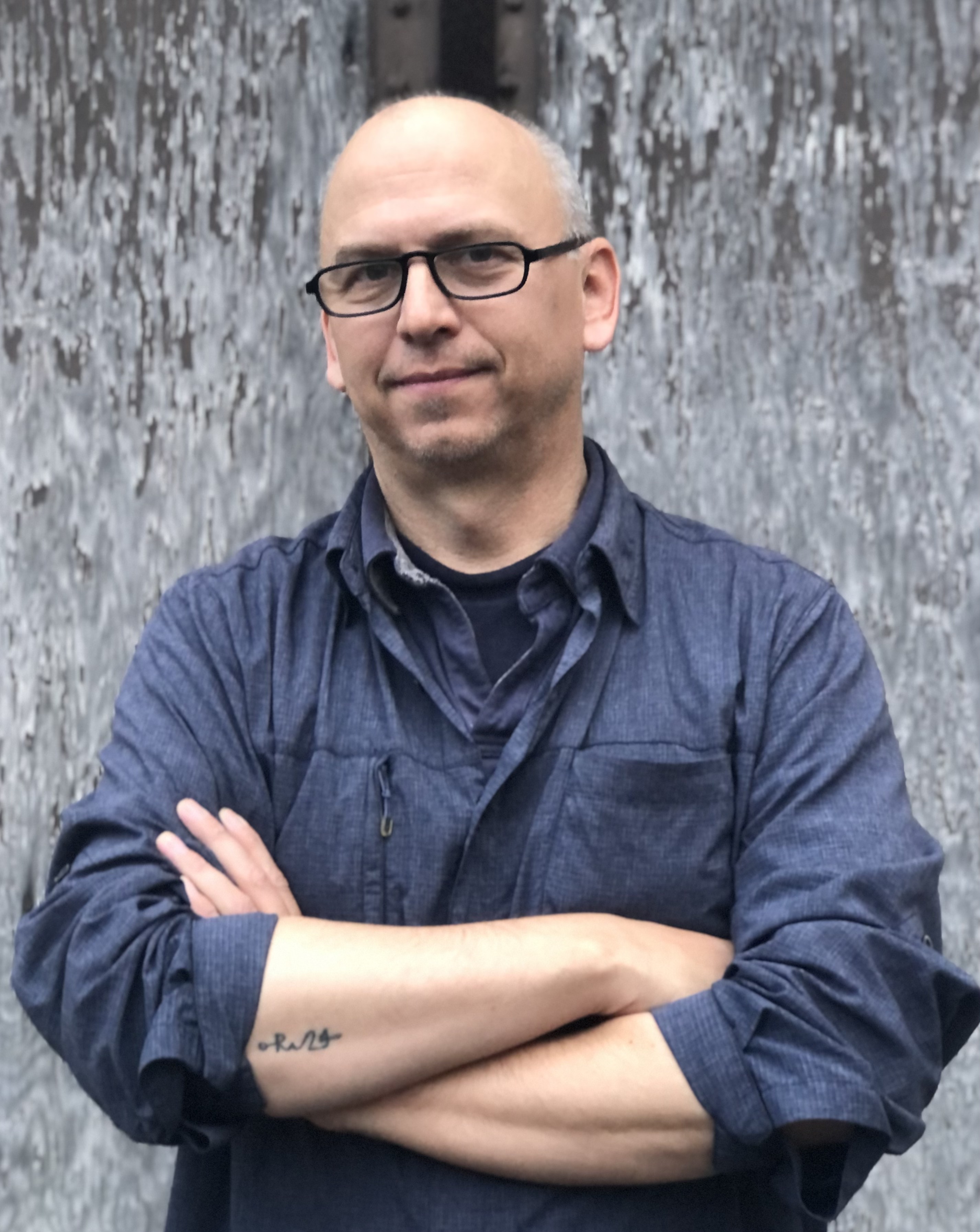 Chuck Stebelton stands with his arms crossed in this portrait, dressed in navy blue, looking at the camera