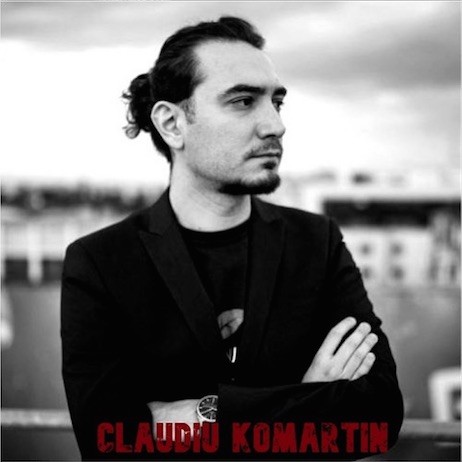 In this black and white portrait, Claudiu Komartin looks to the side with his arms crossed at his chest.