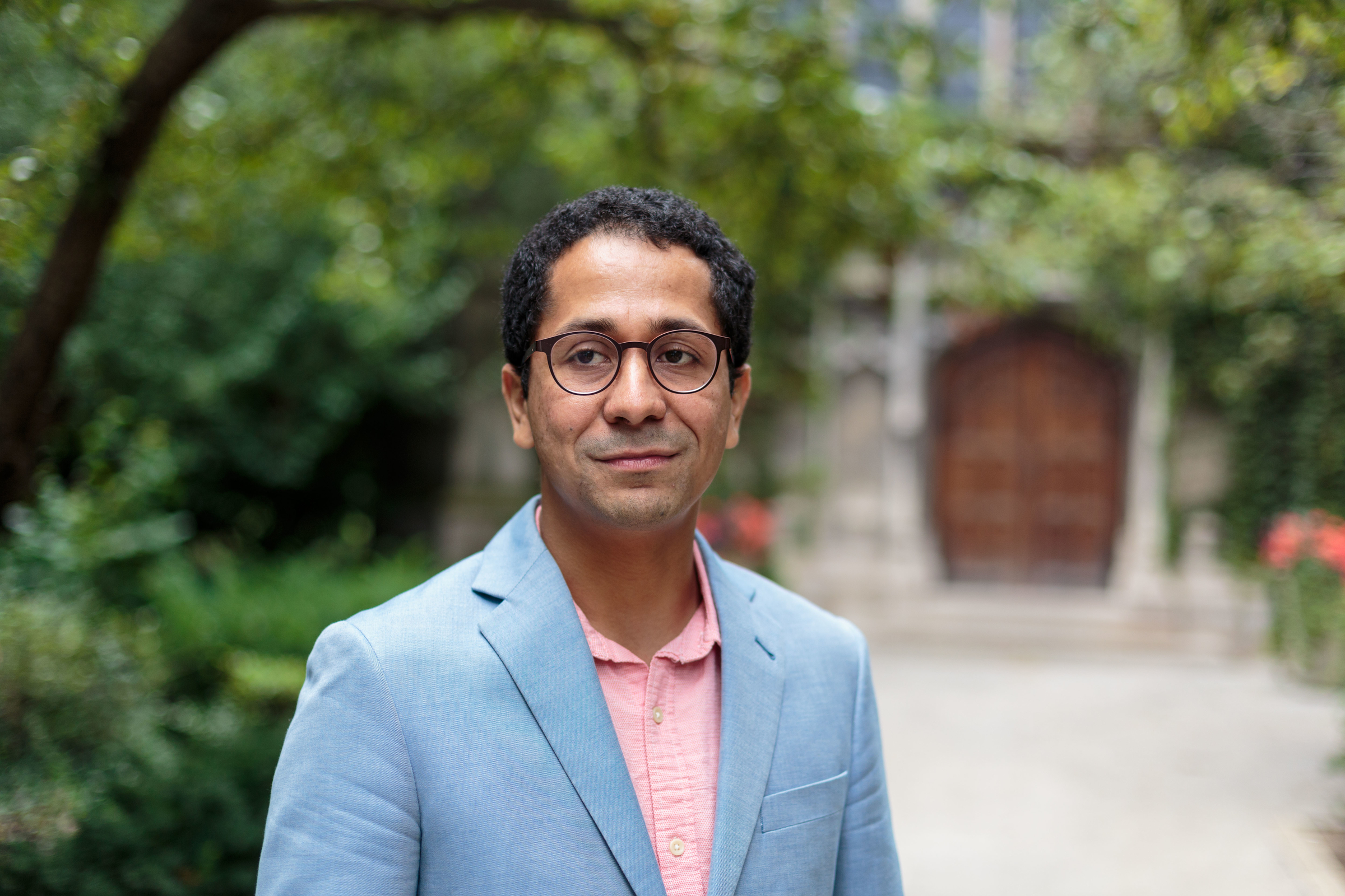 Edgar Garcia is standing outside and smiling, looking slightly to the side of the camera, wearing a light blue suit jacket and pink shirt.