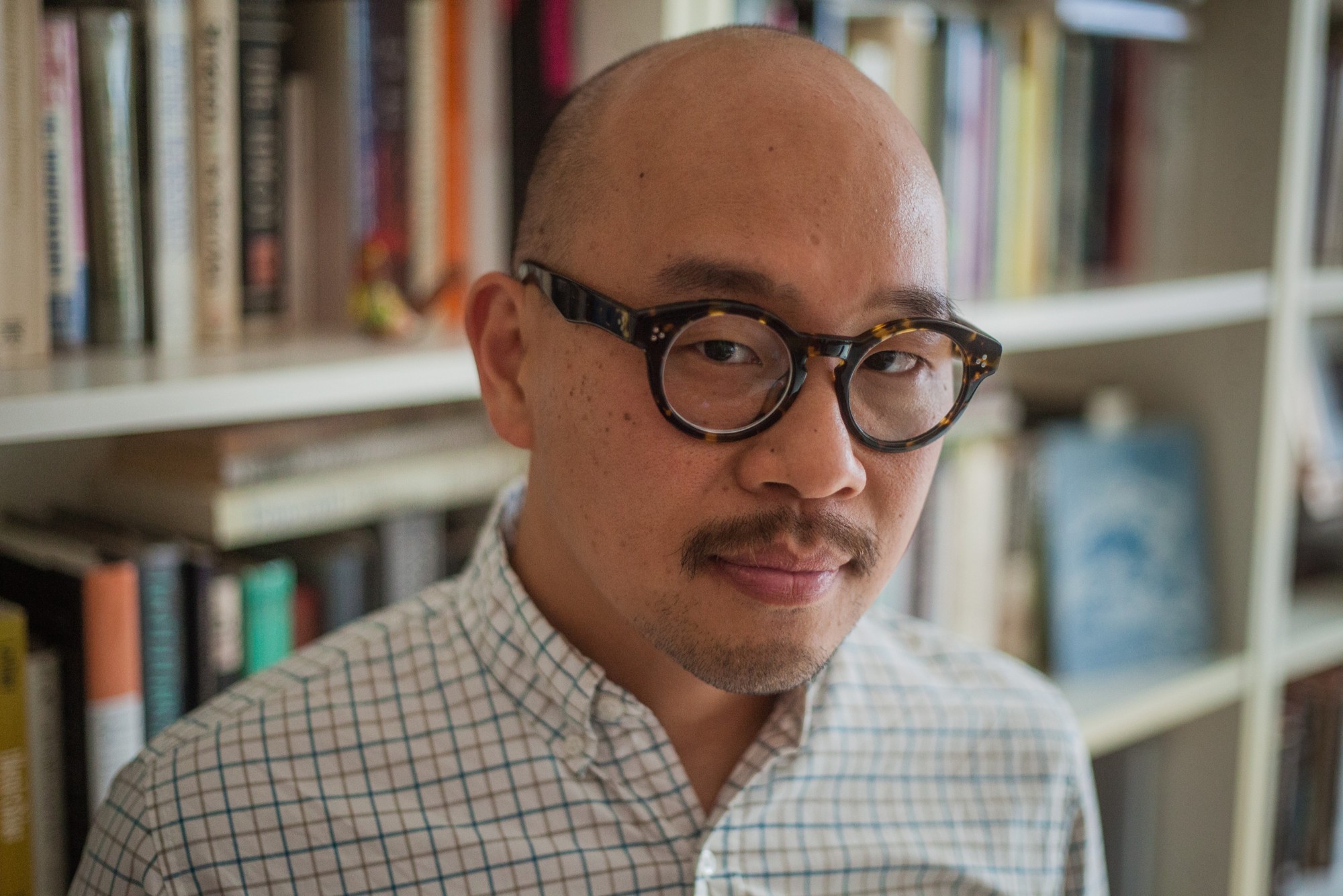 Eugene Lim stands in front of a bookcase, wearing round glasses and a button-up shirt.
