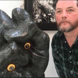 Garrett Caples stands next to a person-size sculpture of a fist with eyes