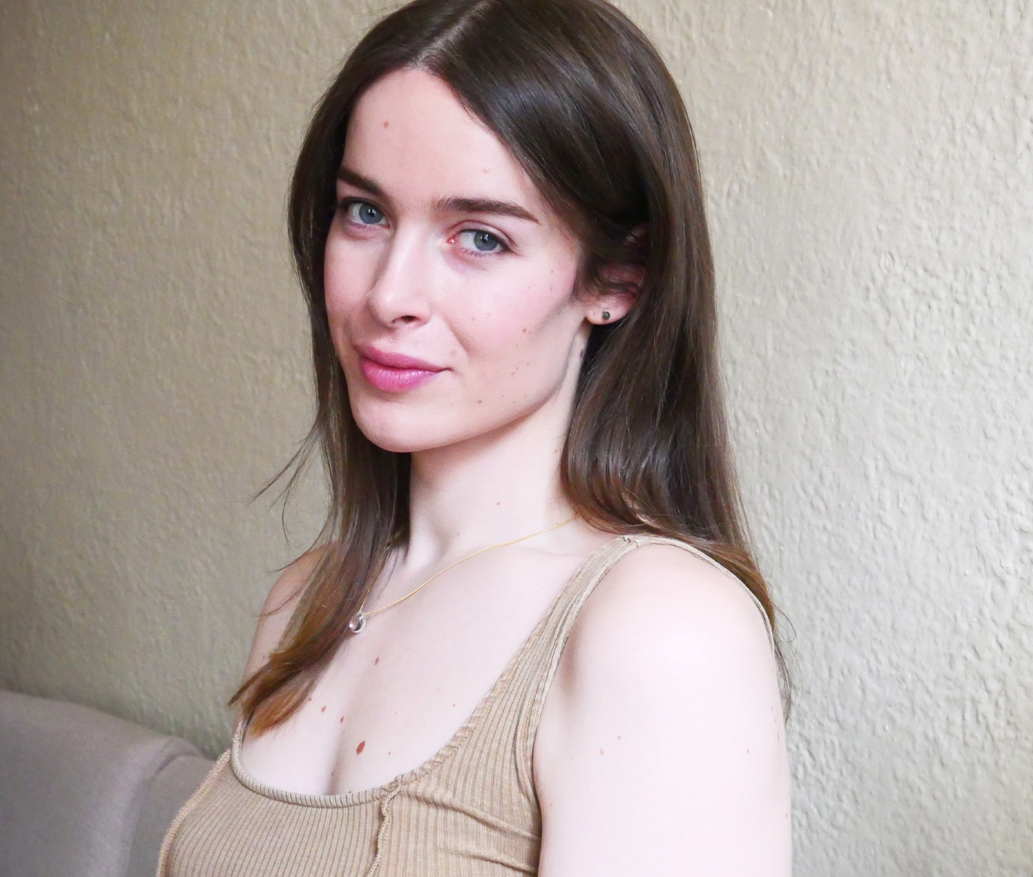 A white woman in her 30s with brown hair wearing a sleeveless, pale taupe top smiles to the camera.