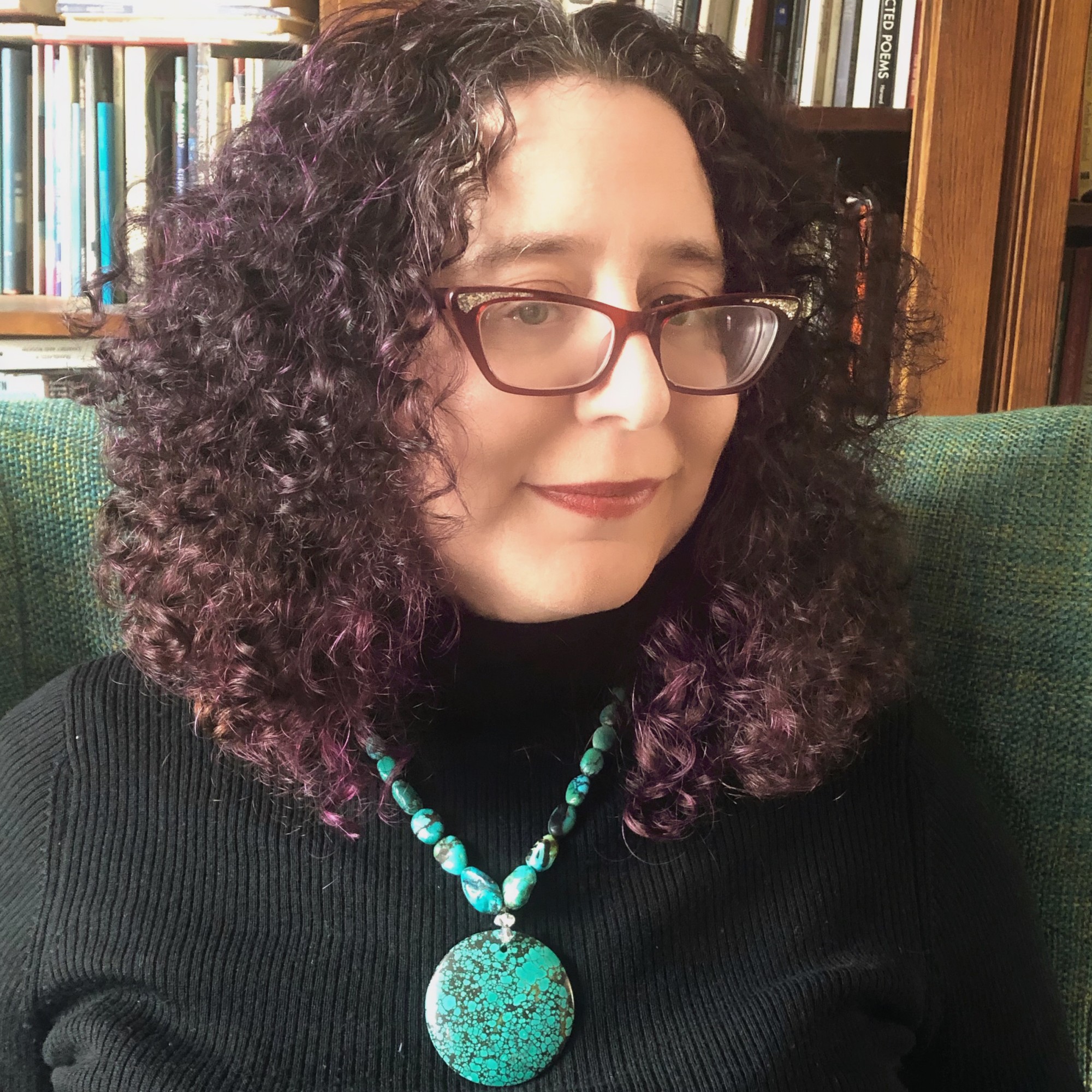 Joanna Fuhrman sits in a green chair, wearing a black turtleneck and large turquoise necklace