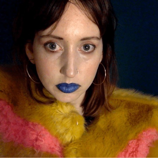 Citron Kelly wears blue lipstick and a pink and orange fur, looking directly into the camera