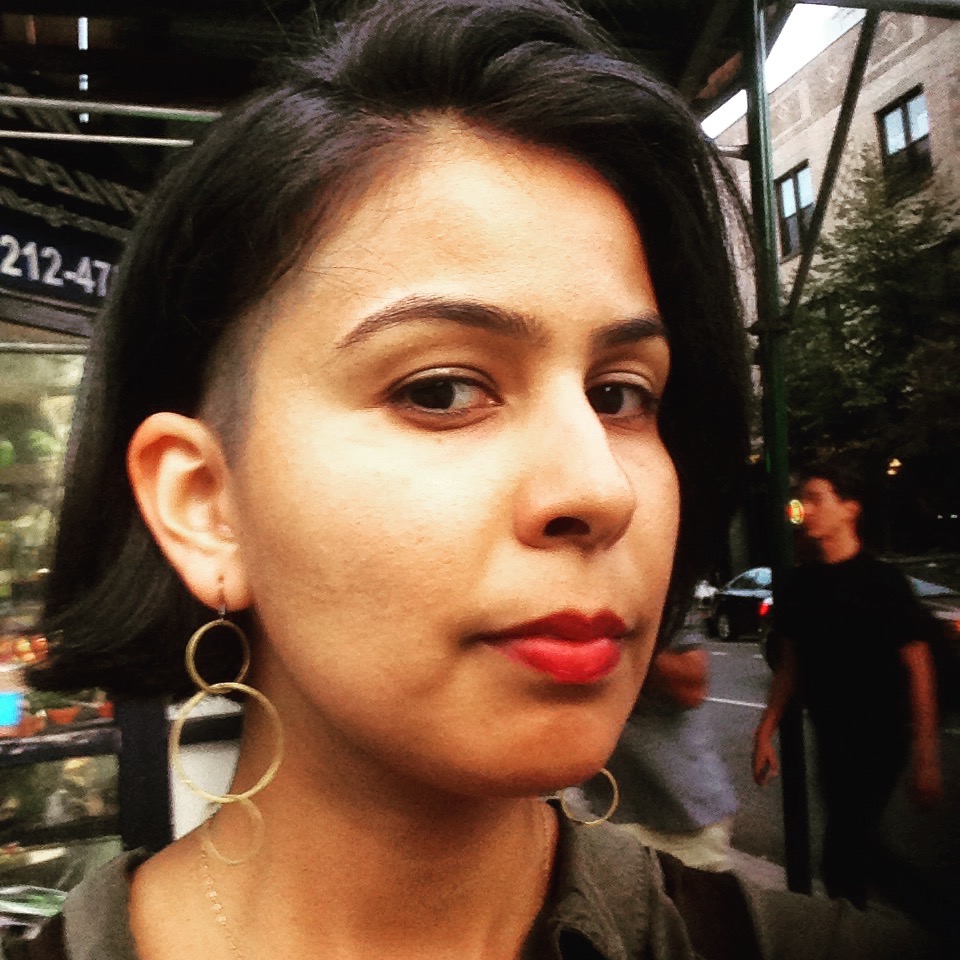 Maryam looks into the camera. She is wearing red lipstick and an earring in her ear.