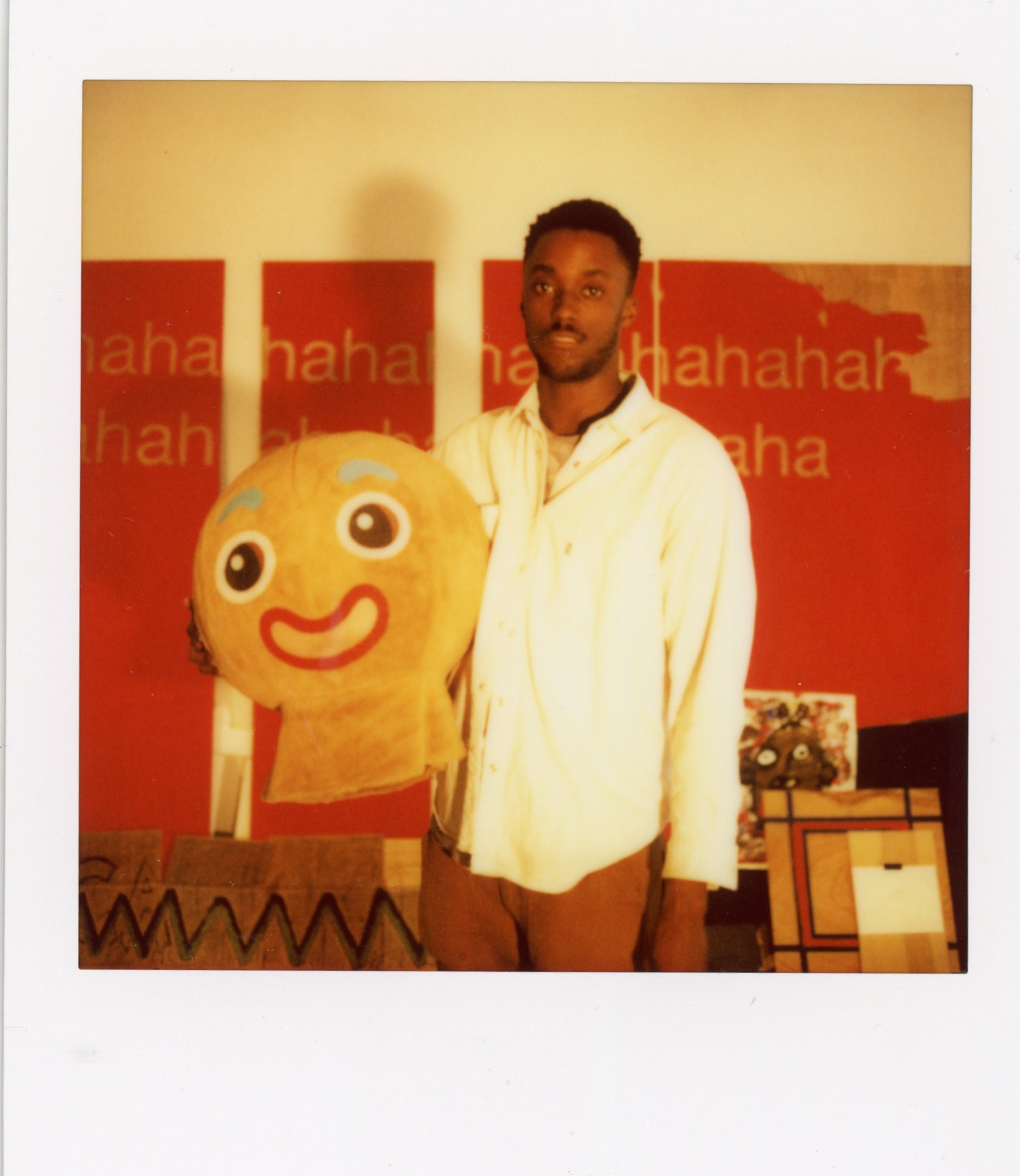 A black man stands in front of a red wall holding the head of a Gingerbread Man costume.