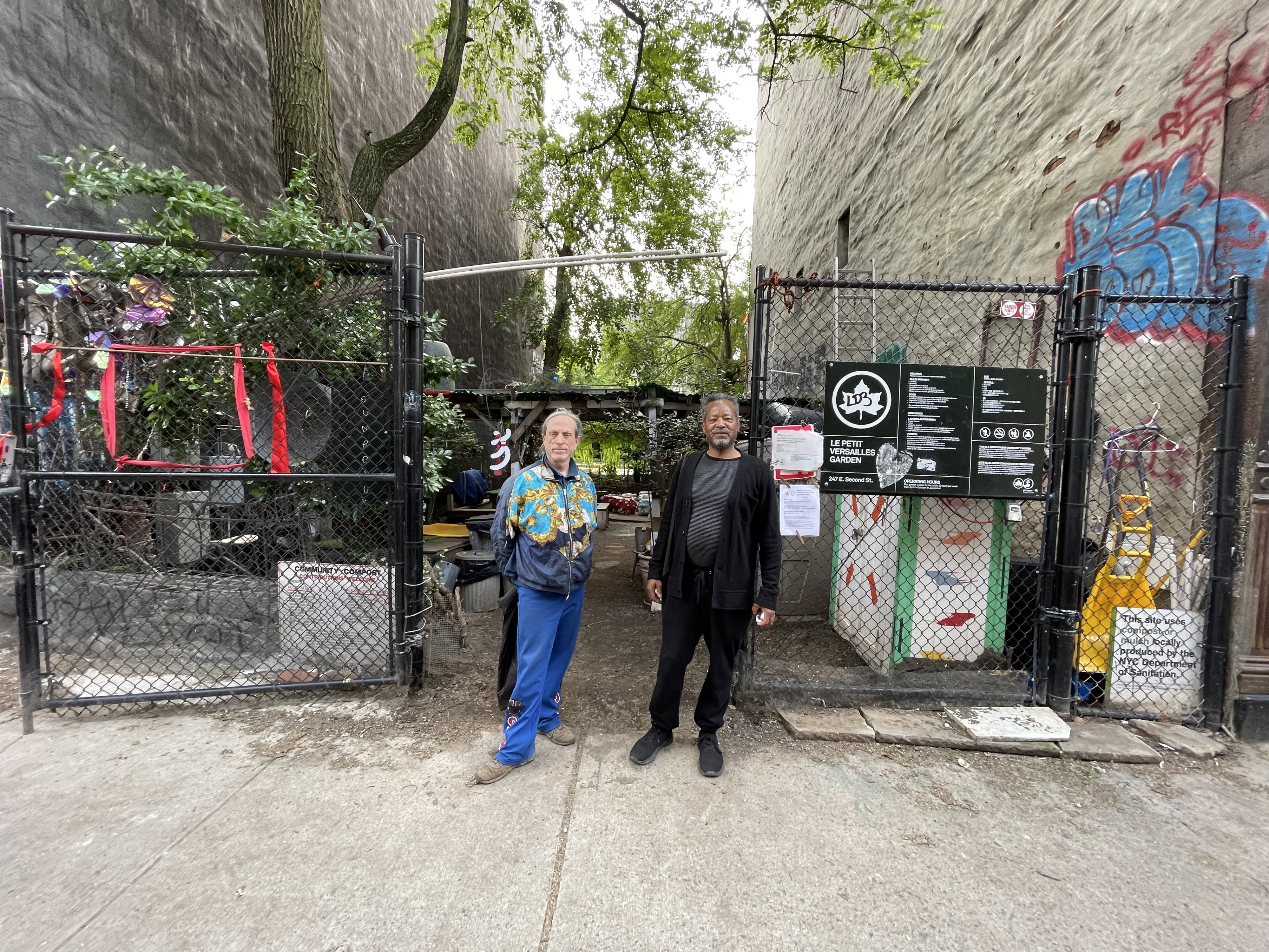 Photograph of artists Jack Waters on left and Peter Cramer on right standing in front of Le Petit Versailles garden that they co-founded in 1995.