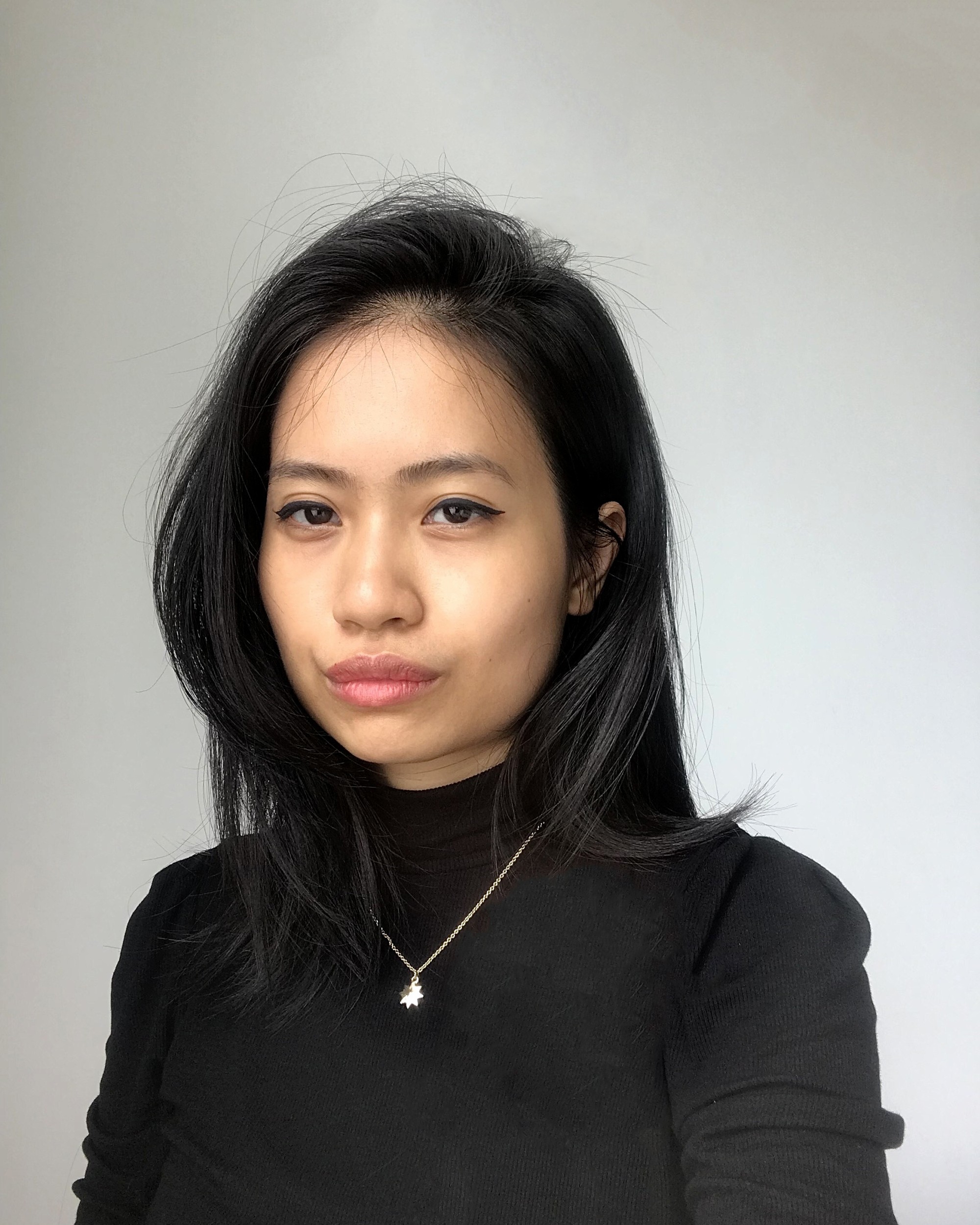 Quyên Nguyễn-Hoàng wears a black turtleneck in front of a white background, looking into the camera