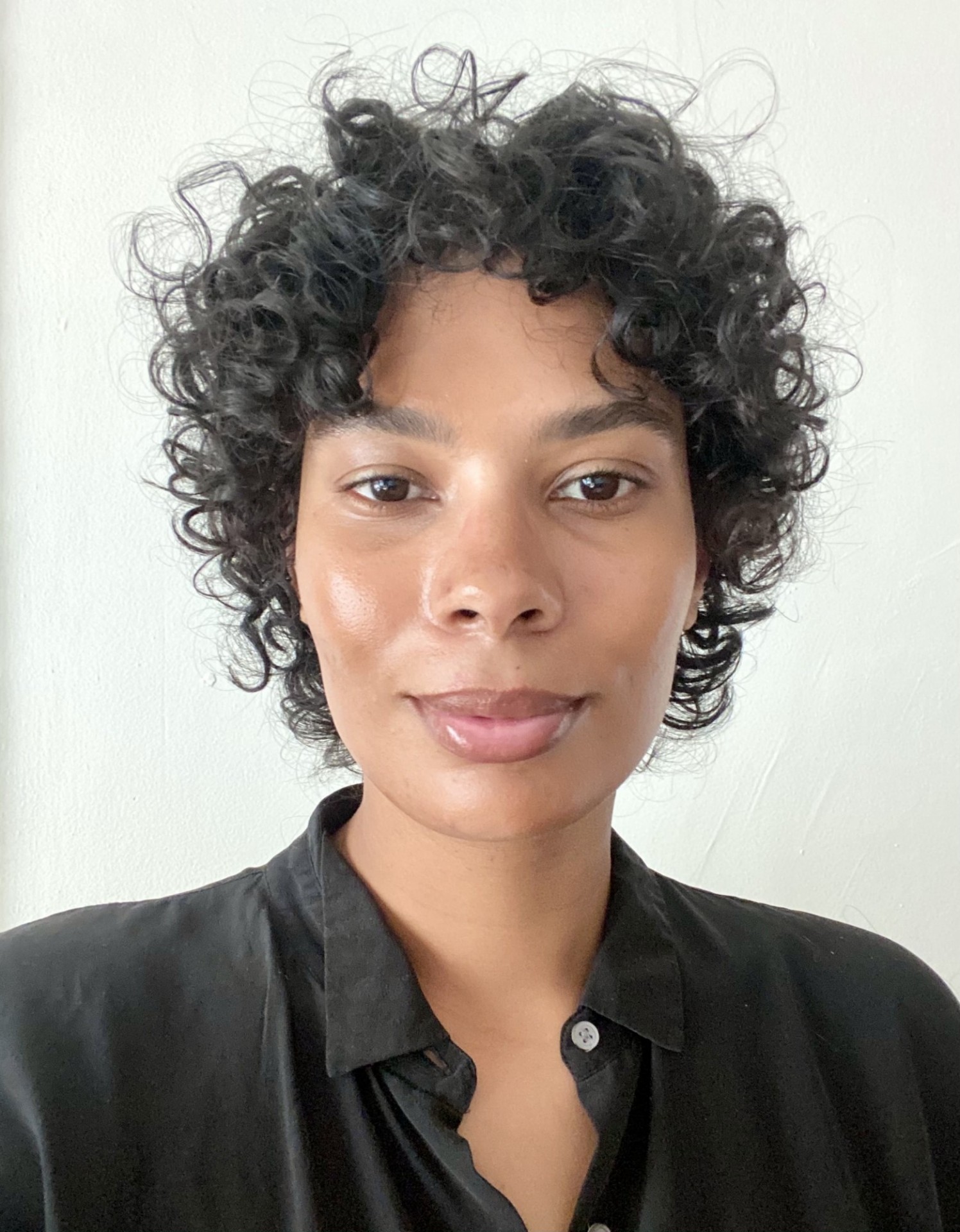 African-American woman with curly hair looking directly at the camera, wearing a collared black shirt.