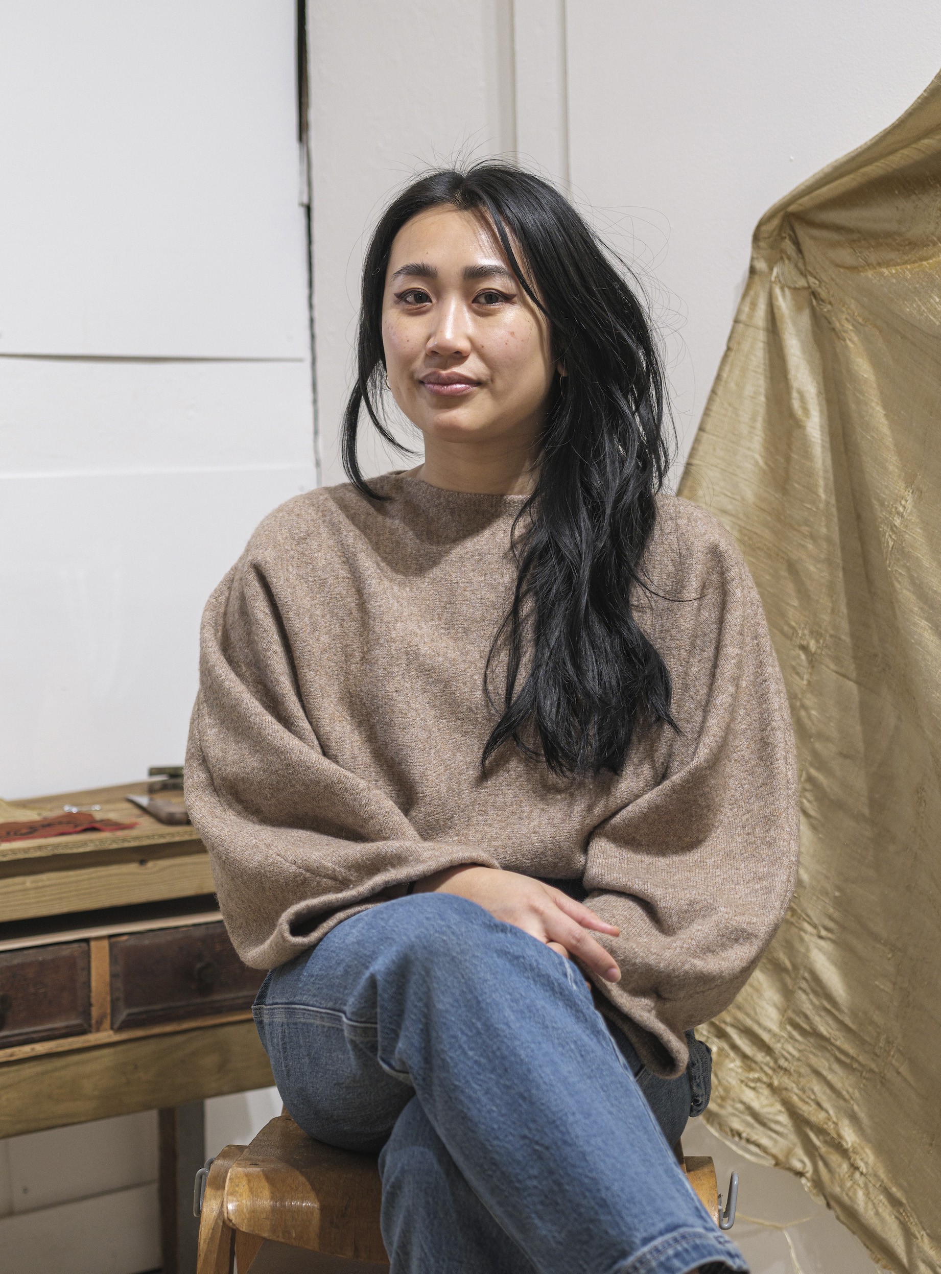 Rachel TonThat is seated, wearing a brow sweater, looking at the camera and smiling softly