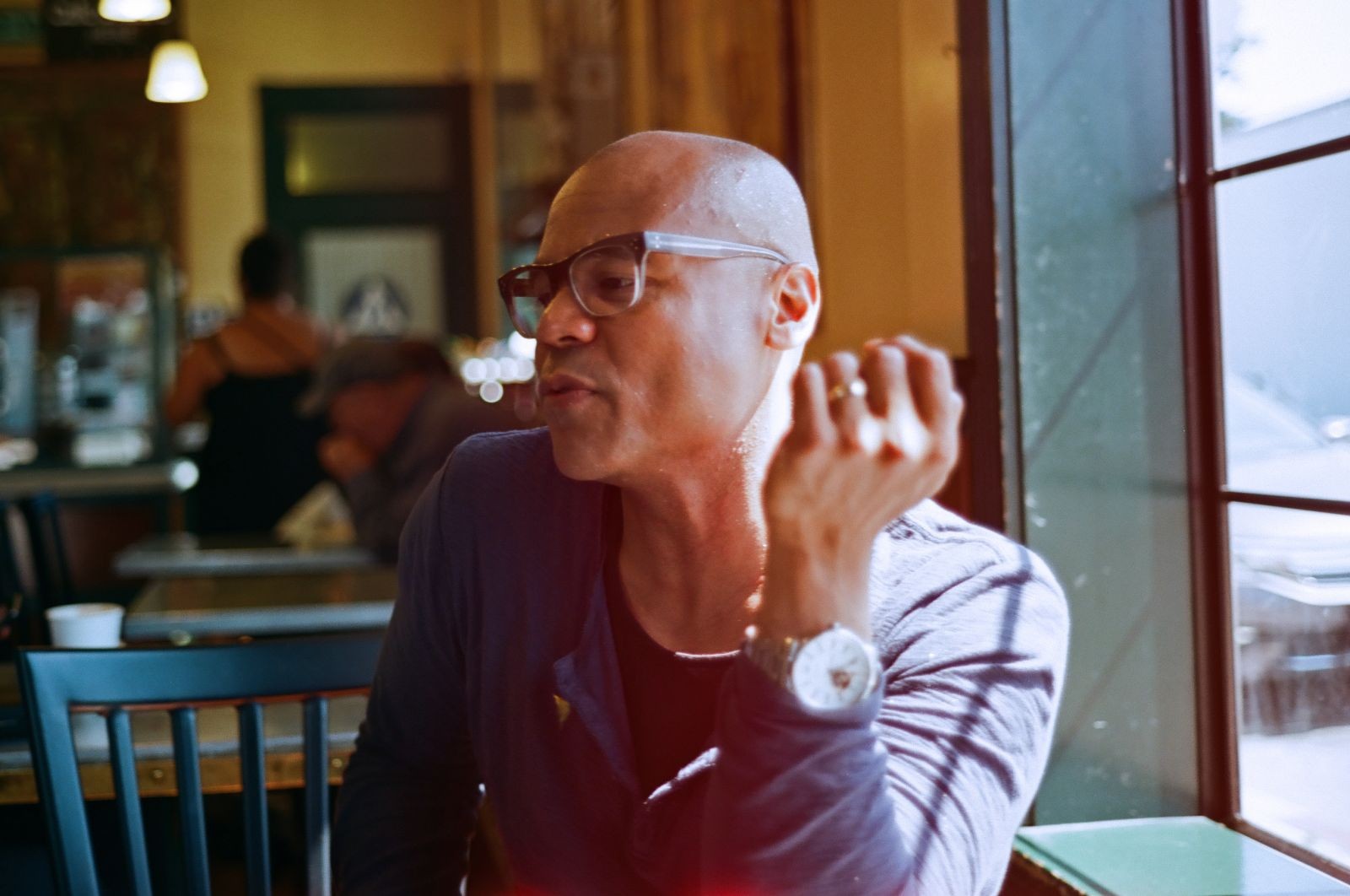 Ronaldo is featured in a landscape-oriented photograph, cropped from the waist up, seated at a table by a window in what appears to be a cafe. His is looking towards the bottom left edge of the frame in three-quarters profile. His left elbow rests on the table and his hand is poised idly in the air slightly in front of and to the side of his face.