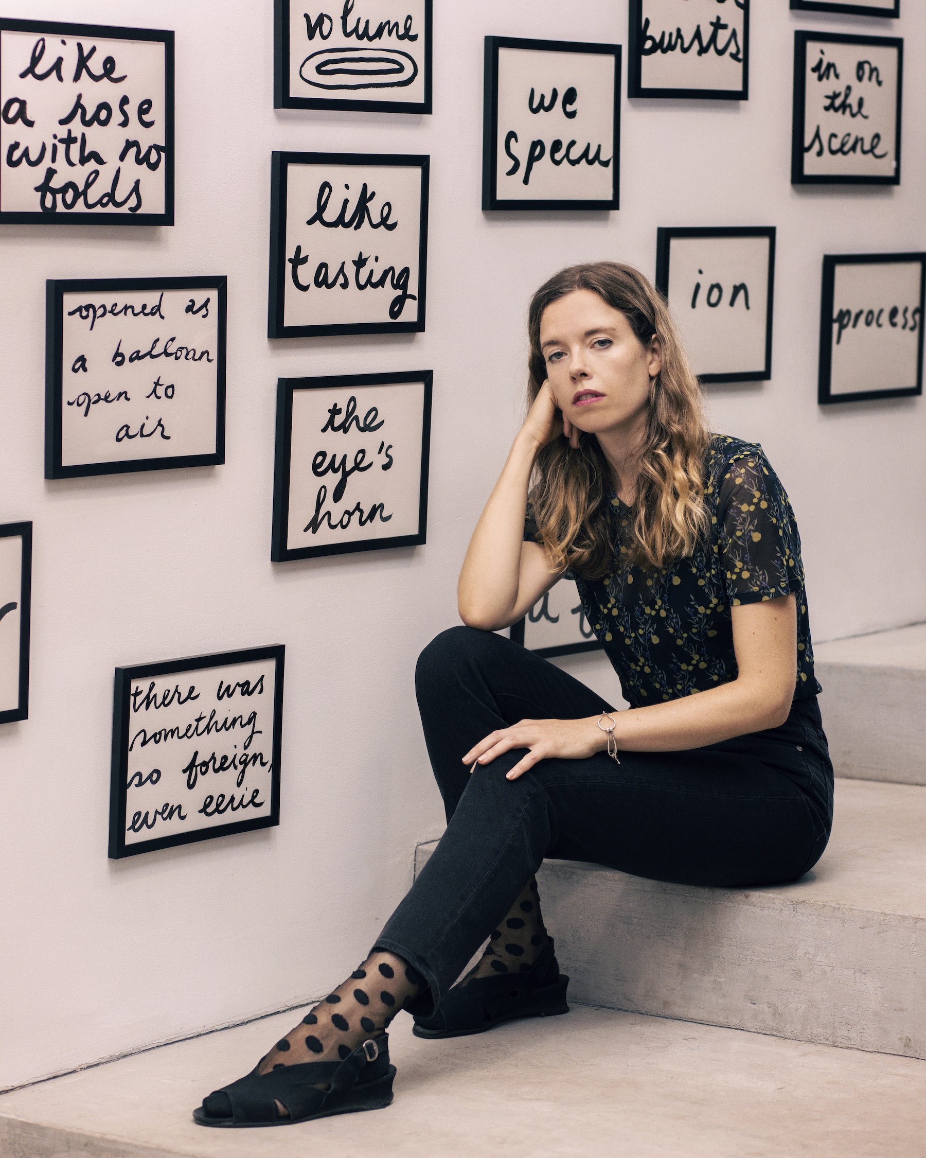 Simone Kearney wears all black, sitting on the stairs at her exhibition, Criers