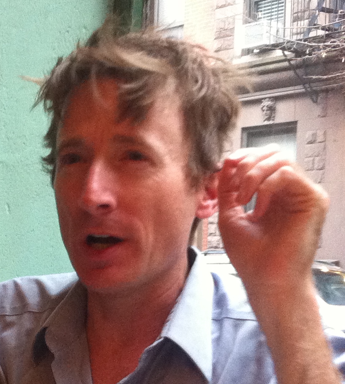 Tim in a blue shirt speaking in a room with a window and blue wall.