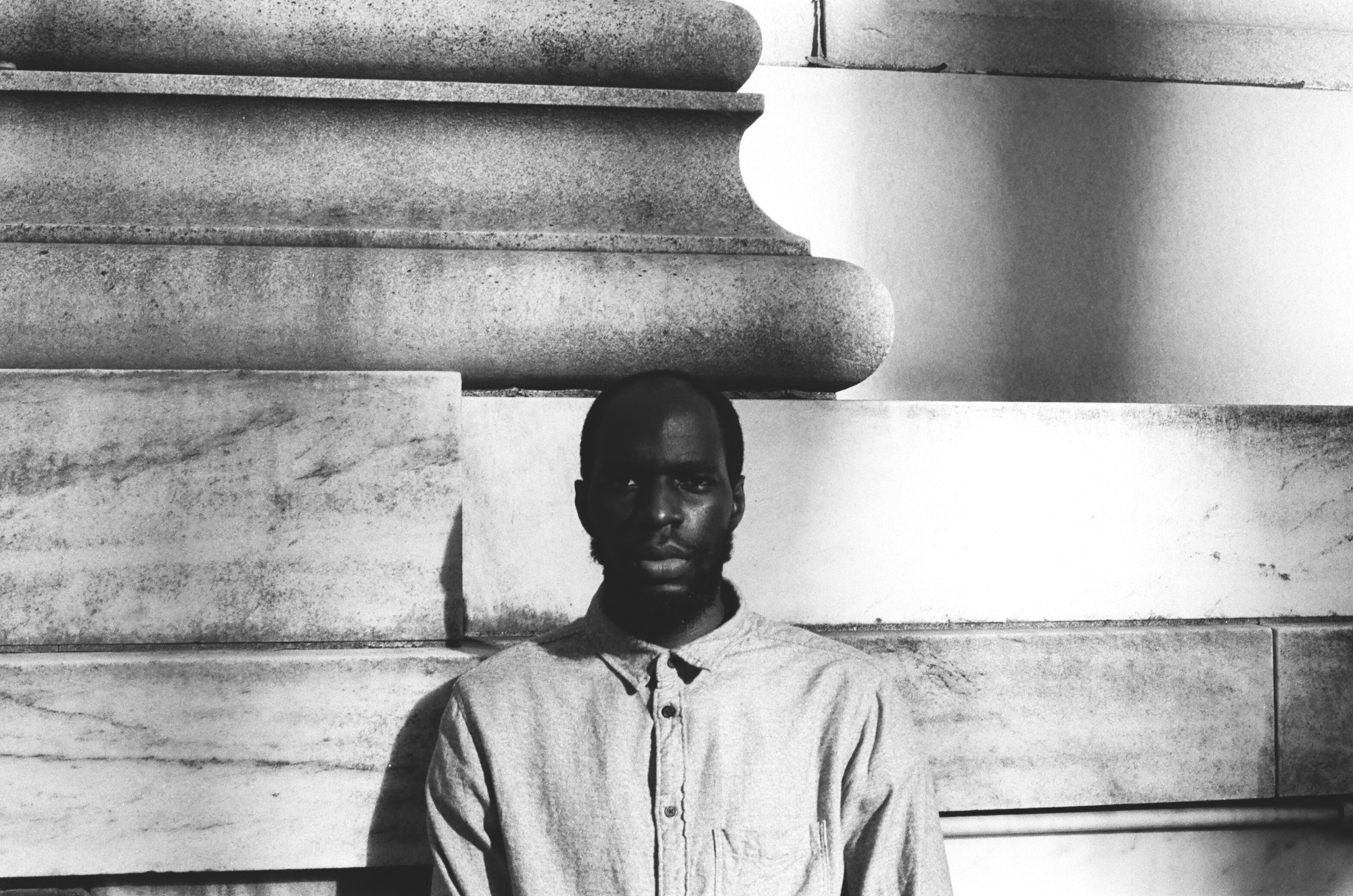 Tobi Kassim is standing in front of a large column in this black and white portrait.