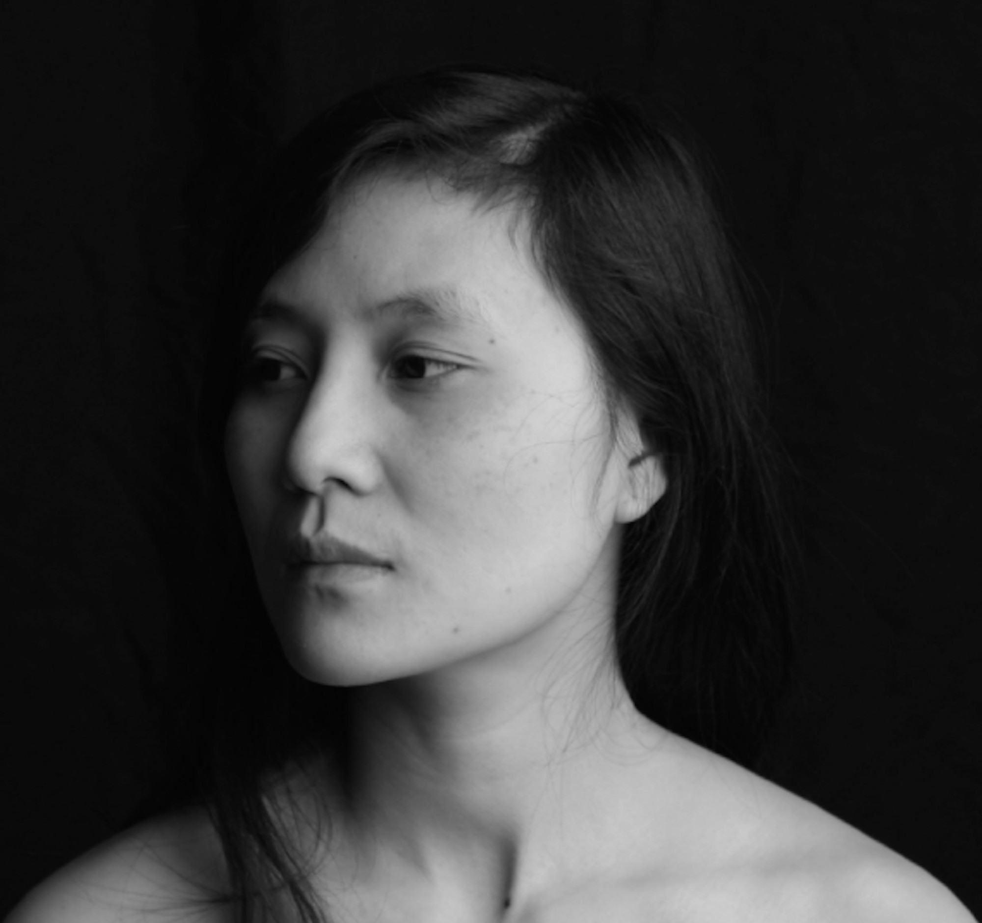 In this black and white portrait, Vi Khi Nao stands in front of a black background, looking off to the side